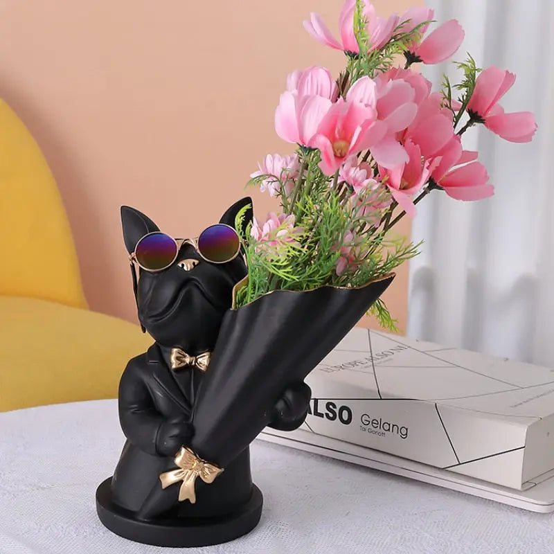 Black dog figurine holding a vase with pink flowers on a light surface.