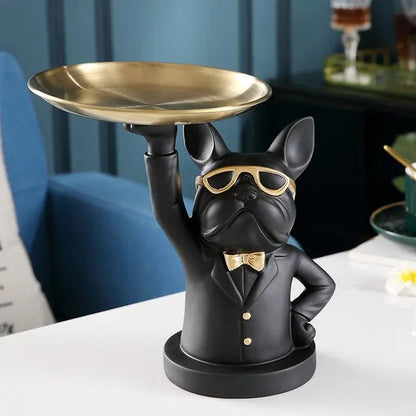 Black dog figurine in a suit holding a gold tray against a blue wall.
