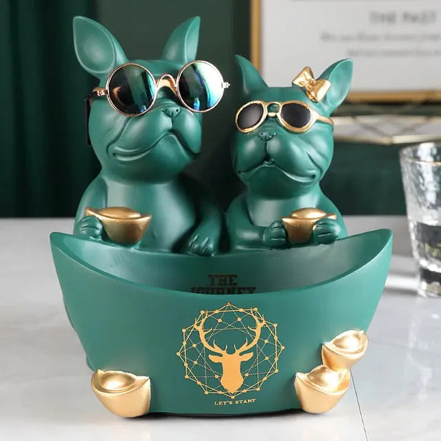 Two green dog figurines with sunglasses on a decorative stand with a glass of water in the background.