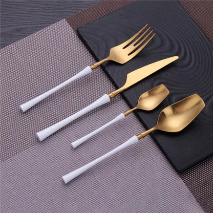 Set of gold cutlery with white handles on a textured surface