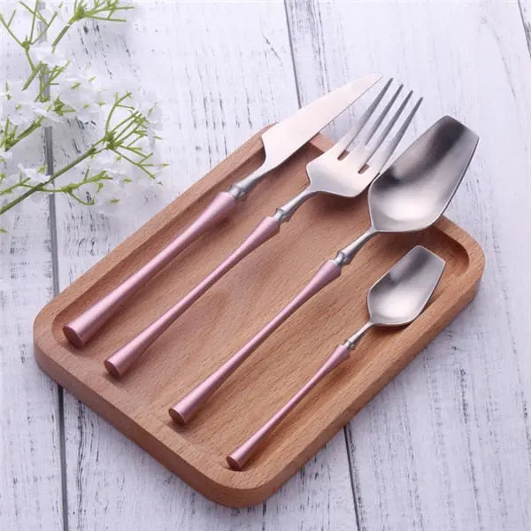 Set of rose gold and silver cutlery on a wooden tray with a white background