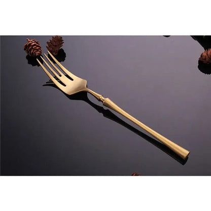 Gold fork on a reflective black surface with pine cones in the background