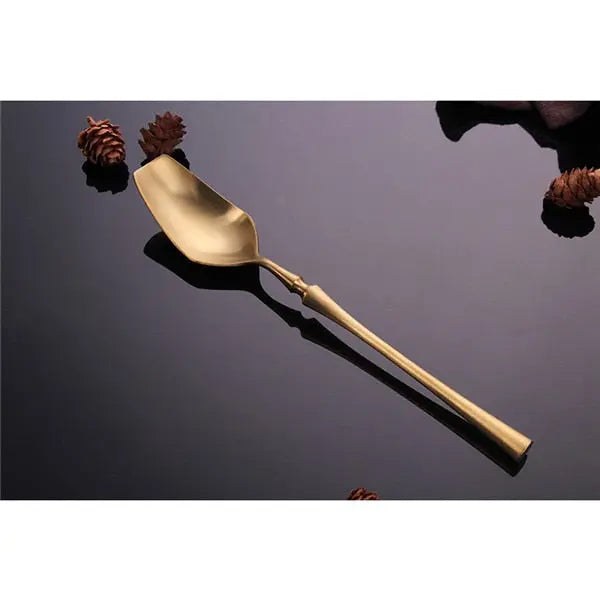 Gold cake server on a reflective black surface with pine cones.