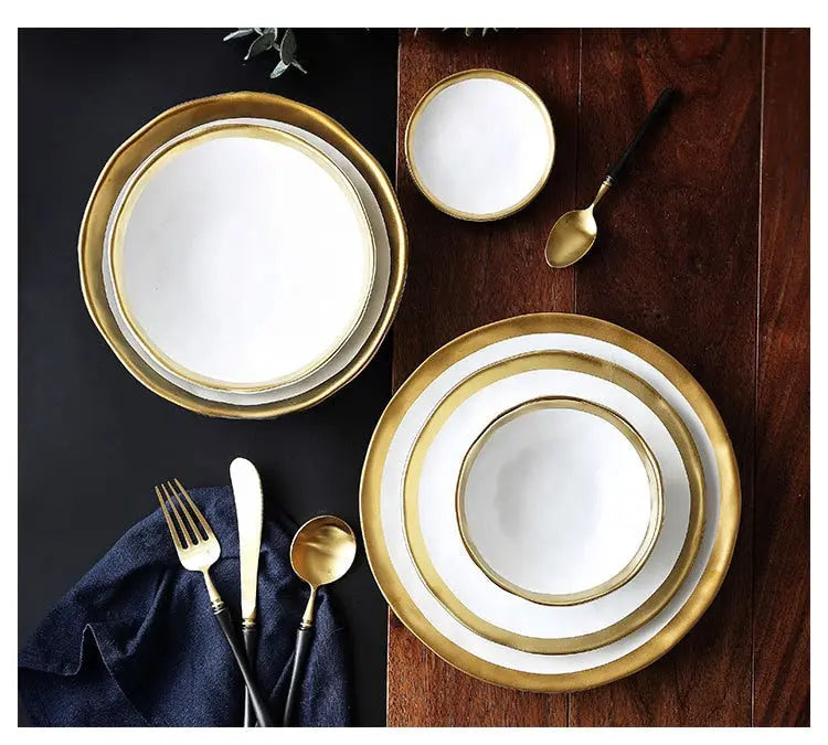 Set of gold-rimmed white plates on a wooden table with silverware.