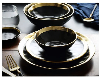 Black dinnerware set with gold rims on a wooden table.