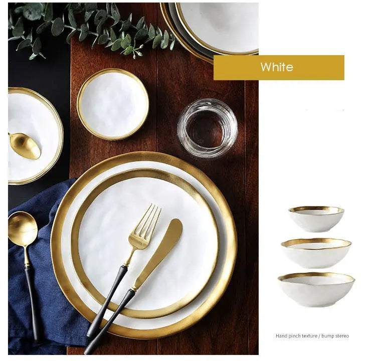 White dinnerware set with gold rims on a wooden table, including plates, bowls, and cutlery.