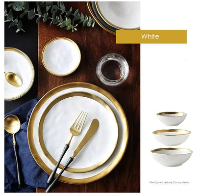 White dinnerware set with gold rims on a wooden table, including plates, bowls, and cutlery.