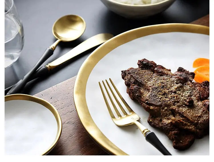 Steak on a white plate with gold rim, accompanied by a fork and knife on a dark surface.