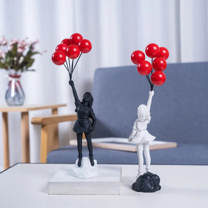 Two black and white figurines holding red balloons on a table with a blurred background.