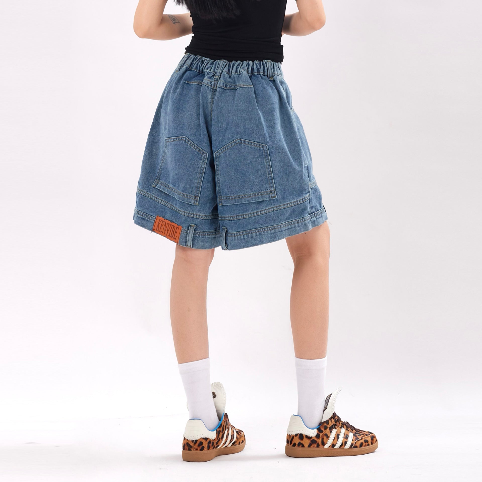 Person wearing a black top, blue denim shorts, and leopard print shoes on a white background