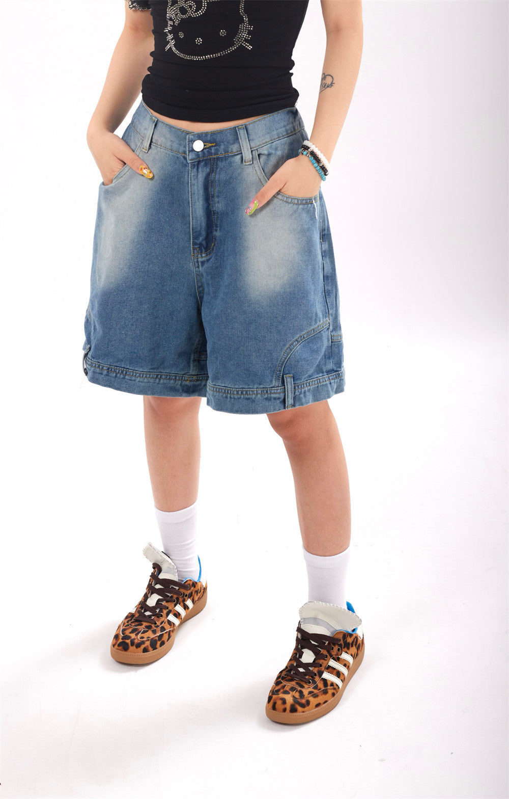 Person wearing blue denim shorts, black top, and leopard print shoes on a white background
