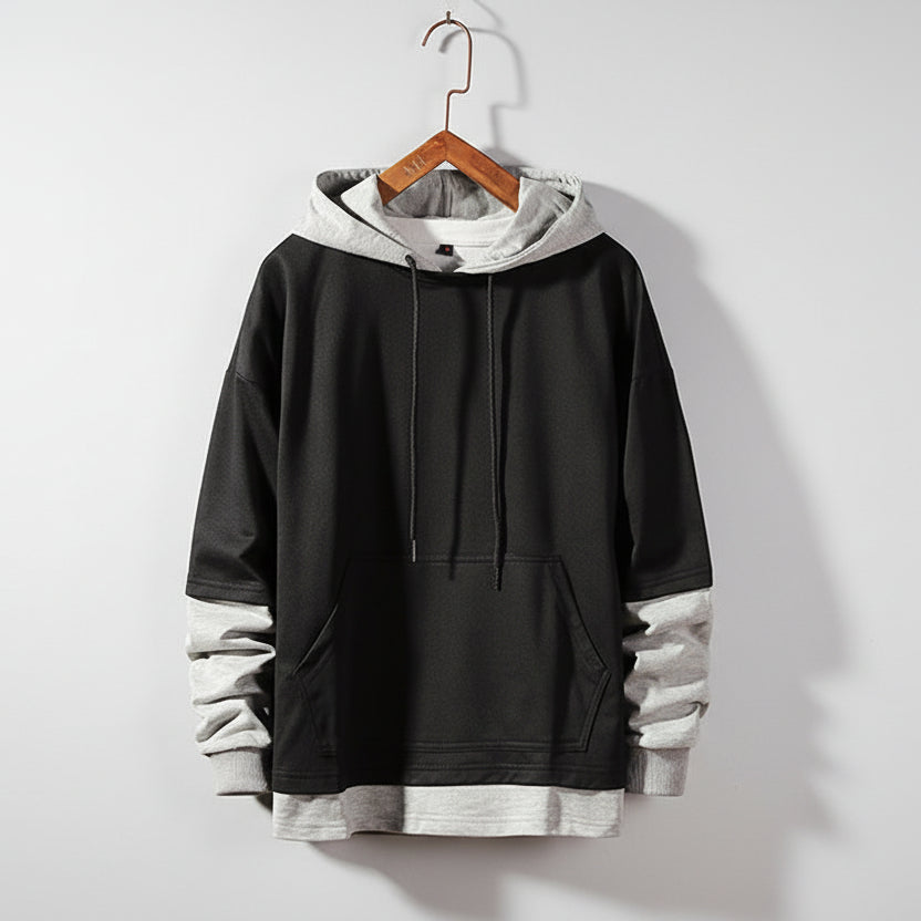 Black and gray hoodie on a wooden hanger against a textured gray wall.