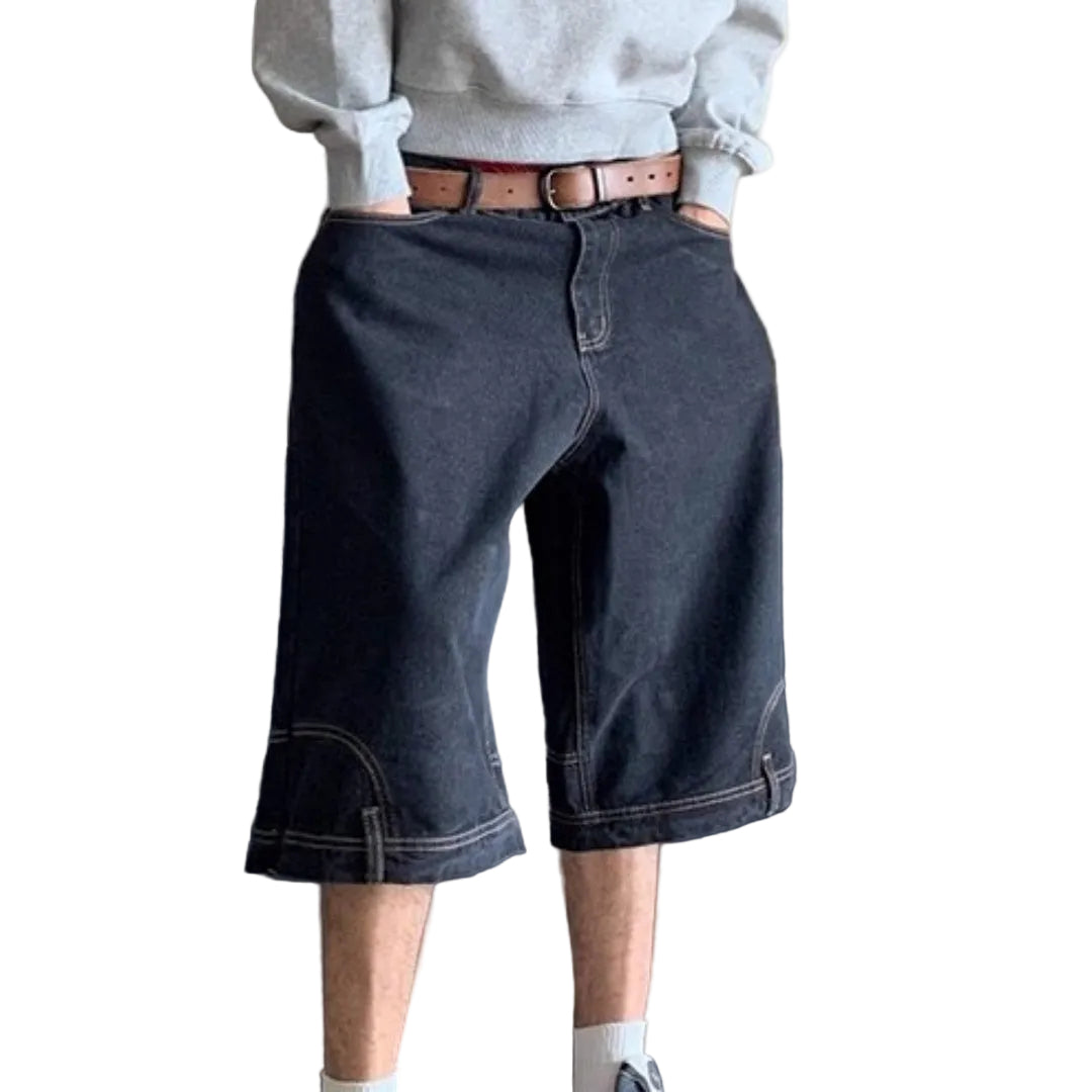 Person wearing dark denim shorts with a gray sweatshirt and brown belt, standing against a neutral background.
