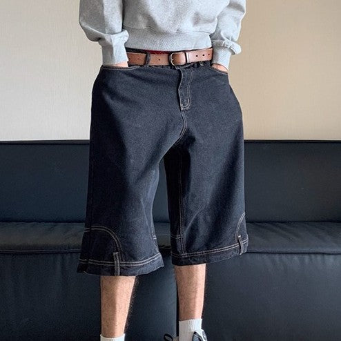 Person wearing dark denim shorts with a gray sweatshirt and brown belt, standing against a neutral background.