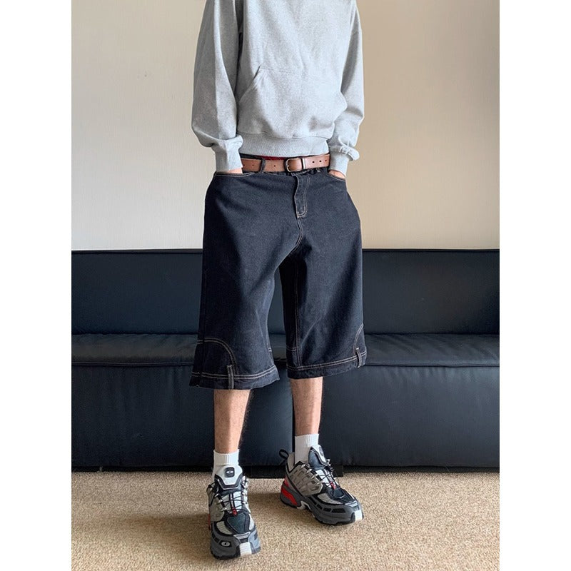 Person wearing a gray sweatshirt, dark shorts, and sneakers standing in front of a black sofa.