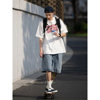 Person skateboarding on a street wearing a white t-shirt, denim shorts, and a black backpack.