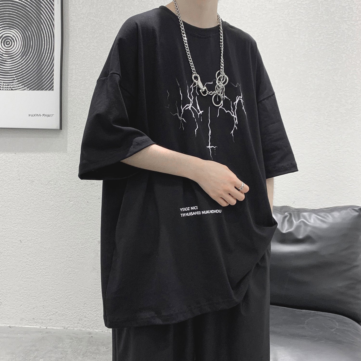 Person wearing a black oversized t-shirt with a graphic design, standing against a neutral background.