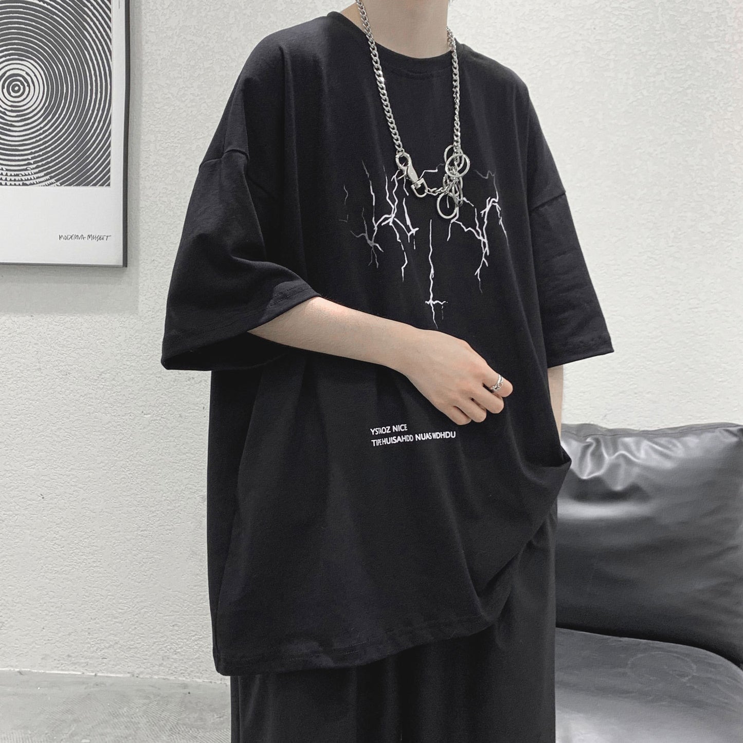 Person wearing a black oversized t-shirt with a graphic design and text, standing against a neutral background.