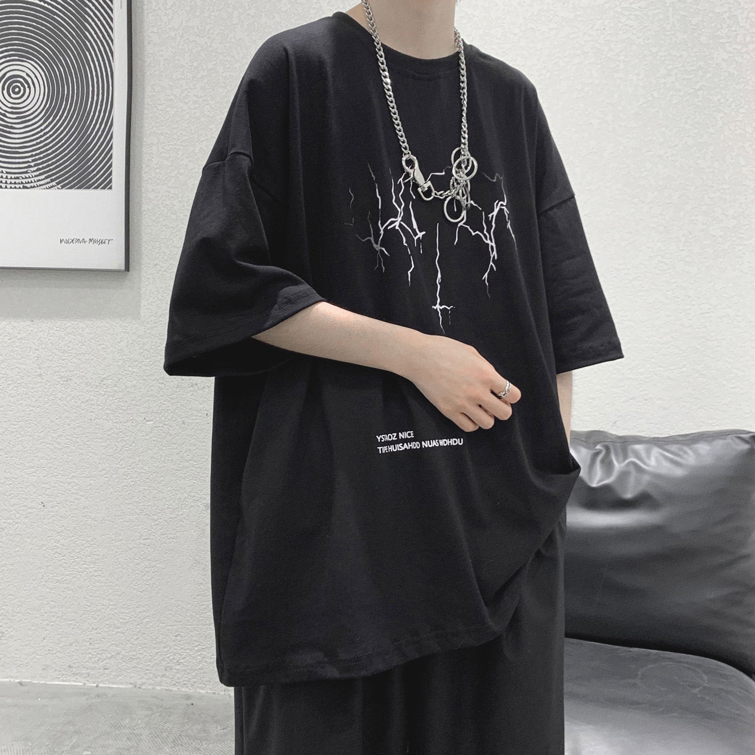 Person wearing a black oversized t-shirt with a graphic design and text, standing against a neutral background.