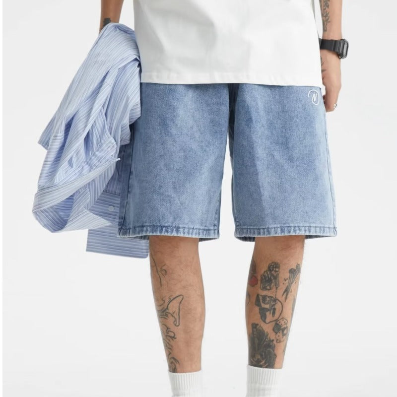 Person wearing light blue denim shorts with a white shirt and tattoos on arms.